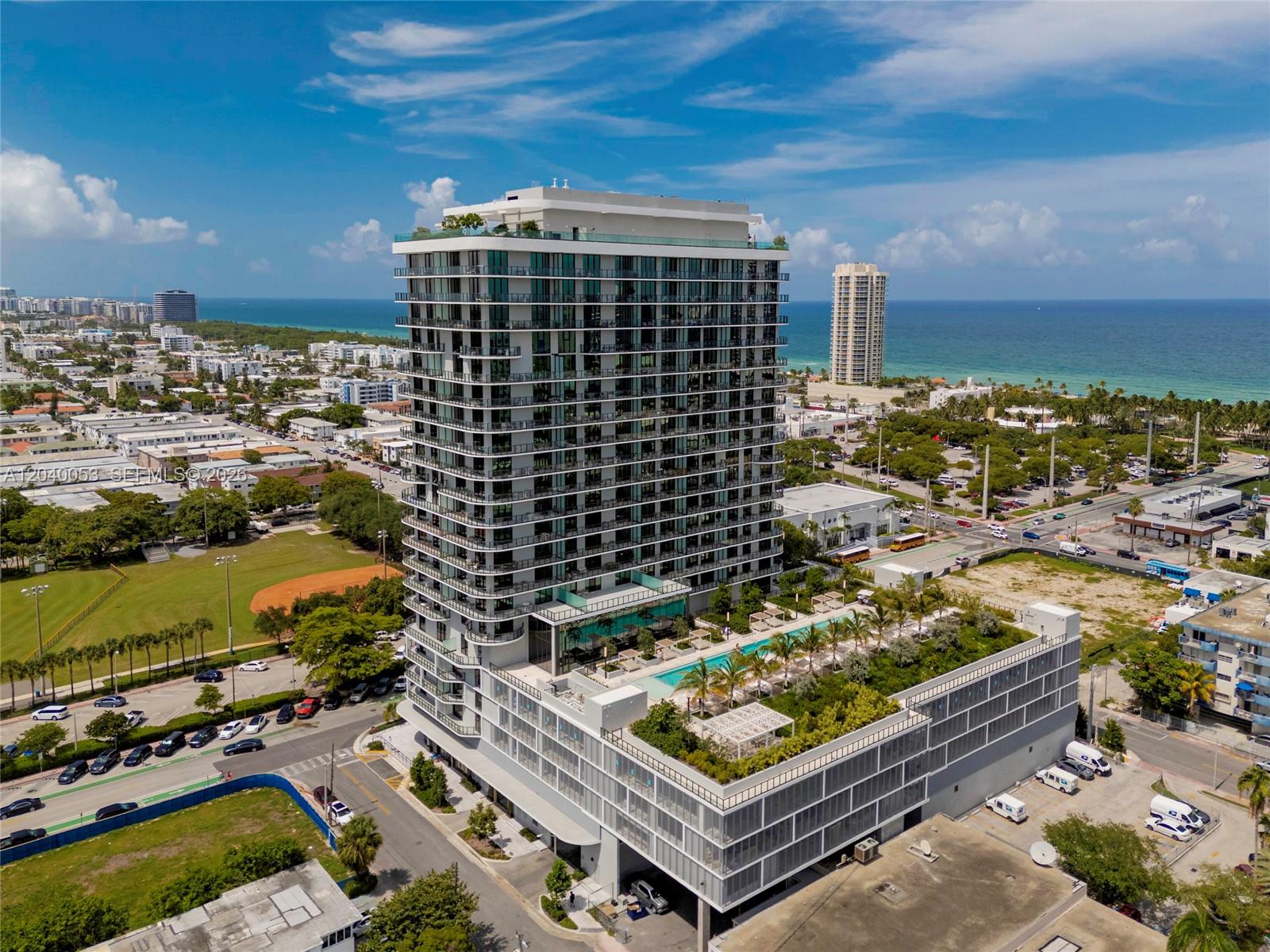 An aerial view shows a modern high-rise apartment building with a rooftop pool and deck — 580 72nd St # 1008, Miami Beach FL 33141, MIAMI BEACH, FL
