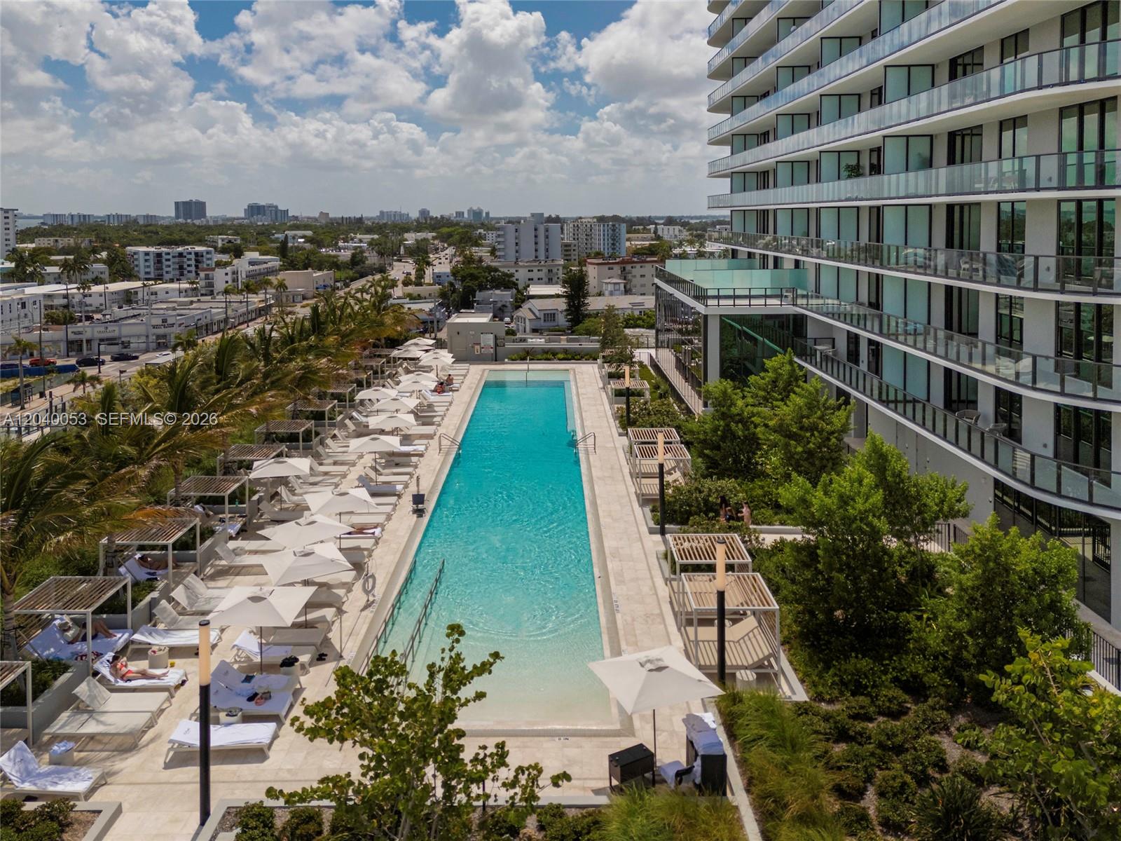 An aerial view shows a long rectangular swimming pool surrounded by lounge chairs and cabanas — 580 72nd St # 1008, Miami Beach FL 33141, MIAMI BEACH, FL