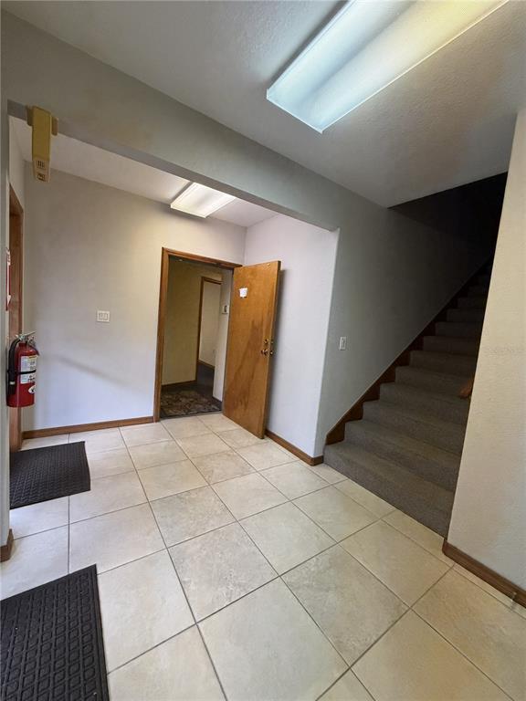 A tiled entryway features a staircase, a wooden door, and a wall-mounted fire extinguisher — 1400 W OAK STREET UNIT C1/D2, KISSIMMEE, FL
