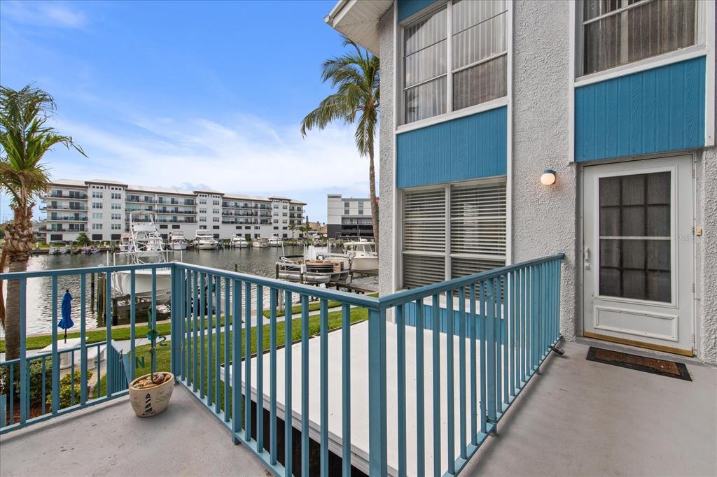 A balcony with blue railings overlooks a marina with boats and a large building — 179 MEDALLION BOULEVARD UNIT H, MADEIRA BEACH, FL