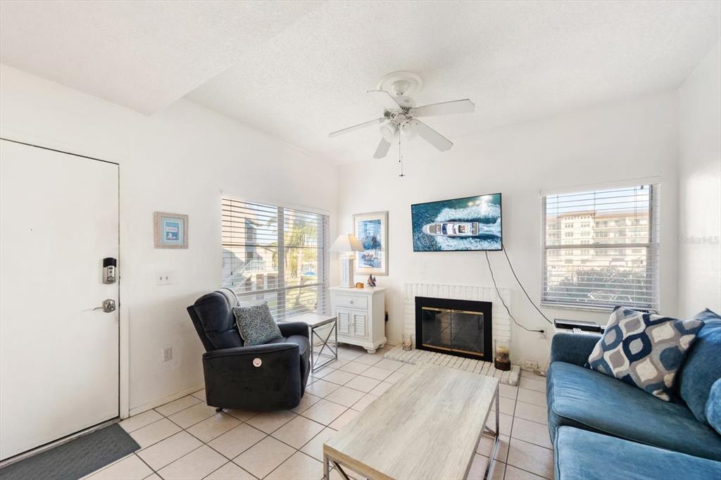 A living room features a fireplace, a ceiling fan, tiled floors, and two windows — 179 MEDALLION BOULEVARD UNIT H, MADEIRA BEACH, FL