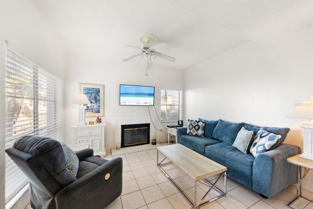 A living room features a blue sofa, a recliner, a fireplace, and tile flooring — 179 MEDALLION BOULEVARD UNIT H, MADEIRA BEACH, FL