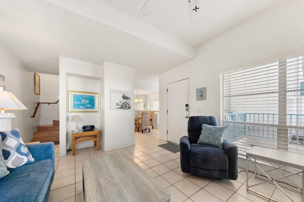 A living room features tile flooring, a blue armchair, a sofa, and a staircase — 179 MEDALLION BOULEVARD UNIT H, MADEIRA BEACH, FL