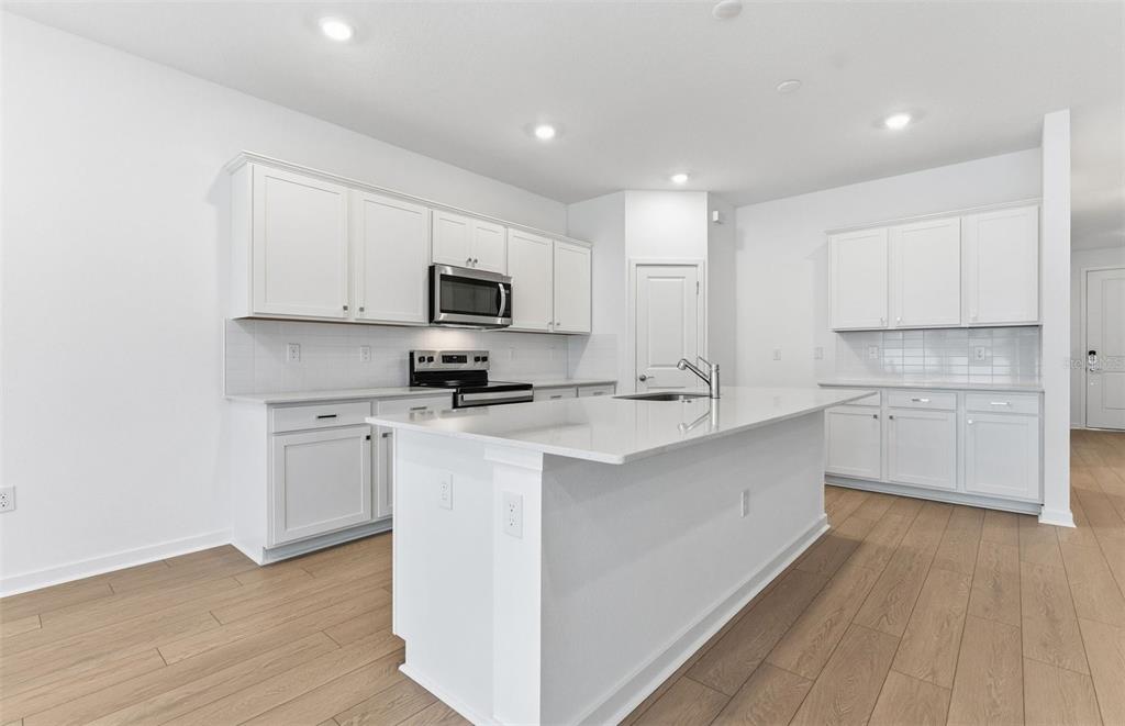 A modern kitchen features white cabinets, a central island with a sink, and wood flooring — 6885 SW 90TH PLACE, OCALA, FL