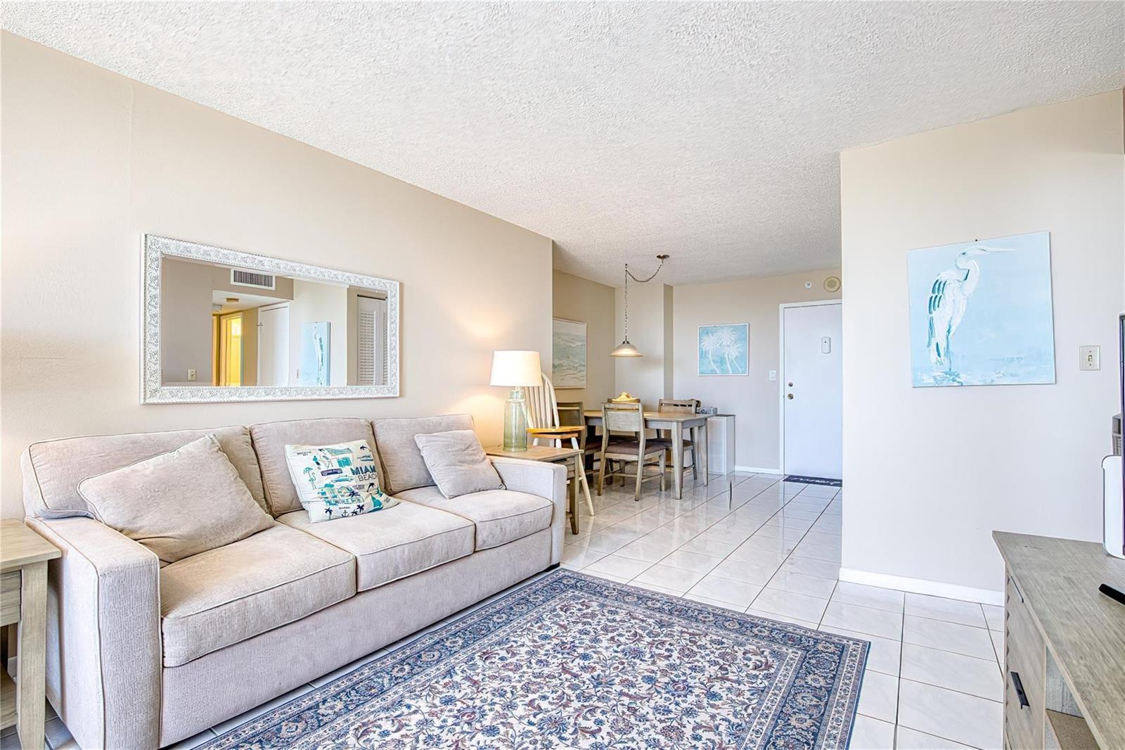 A living room with a beige sofa, tiled floors, a patterned rug, and a dining area — 111 Briny Avenue # 2312, Pompano Beach FL 33062, POMPANO BEACH, FL