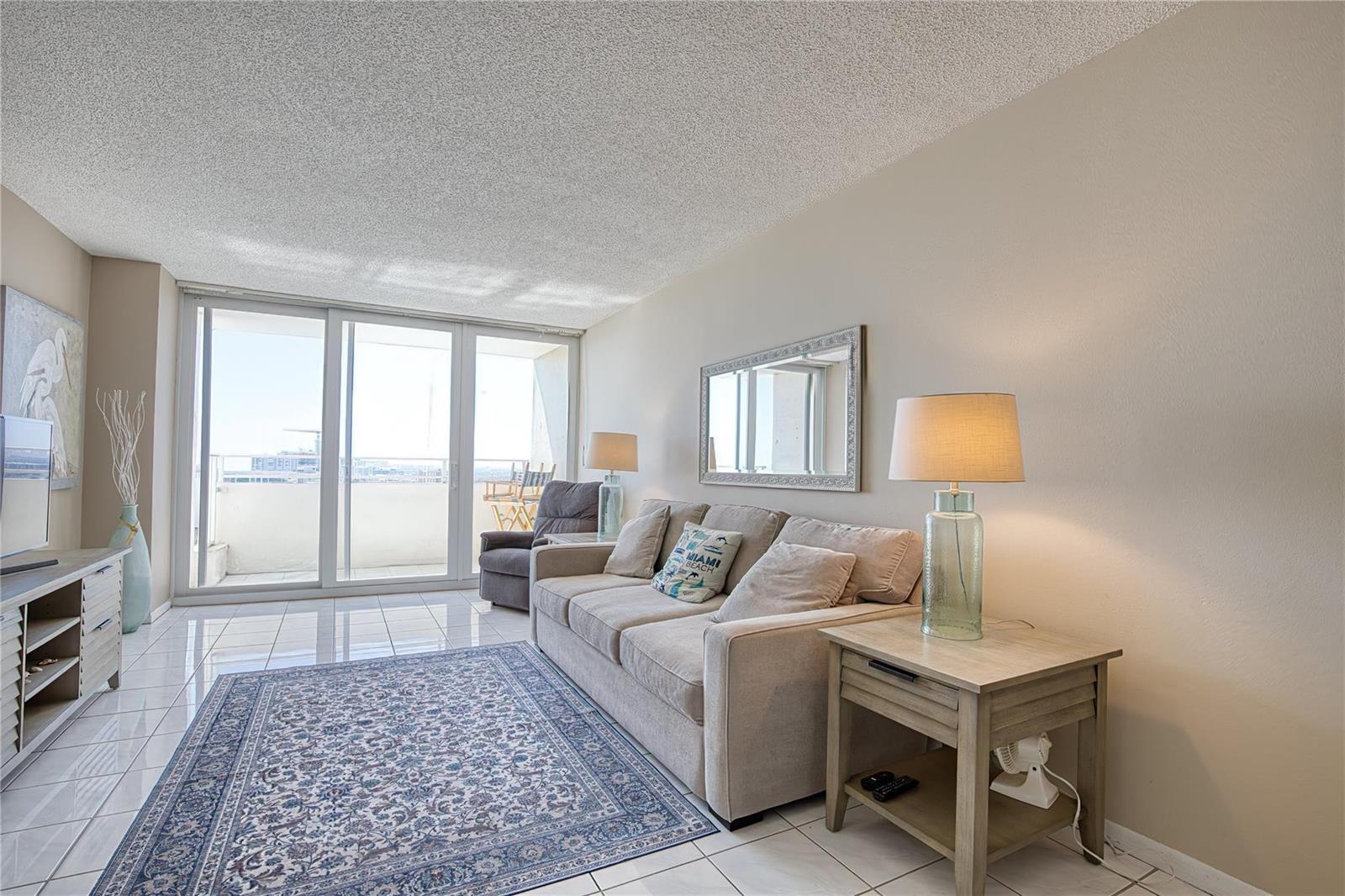 A living room features a beige sofa, a patterned area rug, and a glass balcony door — 111 Briny Avenue # 2312, Pompano Beach FL 33062, POMPANO BEACH, FL
