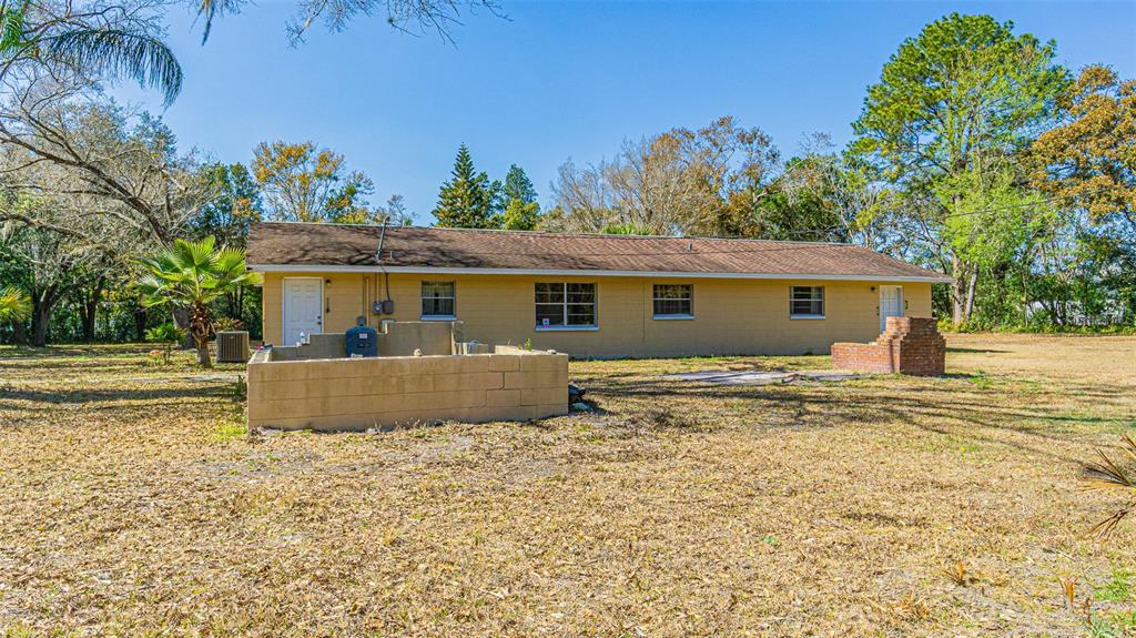 The exterior of a single-story yellow house features a brick chimney and a block wall — 3902 AUTUMN PALM DRIVE, ZEPHYRHILLS, FL