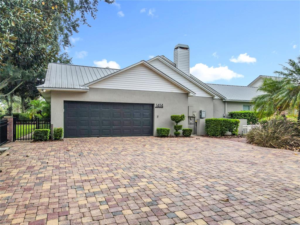 A single-story house with a metal roof, gray stucco walls, and a brick paver driveway — 1414 EDMISTON COURT, AUBURNDALE, FL