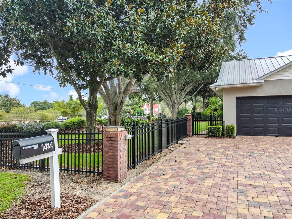 A paved driveway leads to a garage beside a black metal fence and large trees — 1414 EDMISTON COURT, AUBURNDALE, FL