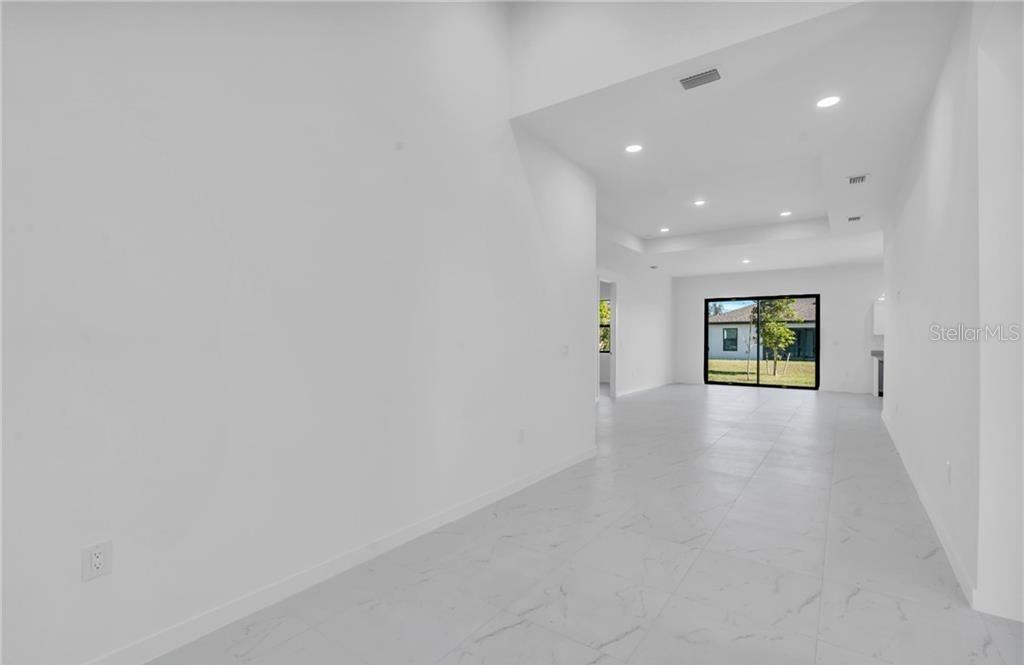 A bright, empty room with white walls, recessed lighting, and light-colored marble-look tile flooring — 1021 CHIQUITA BOULEVARD N, CAPE CORAL, FL