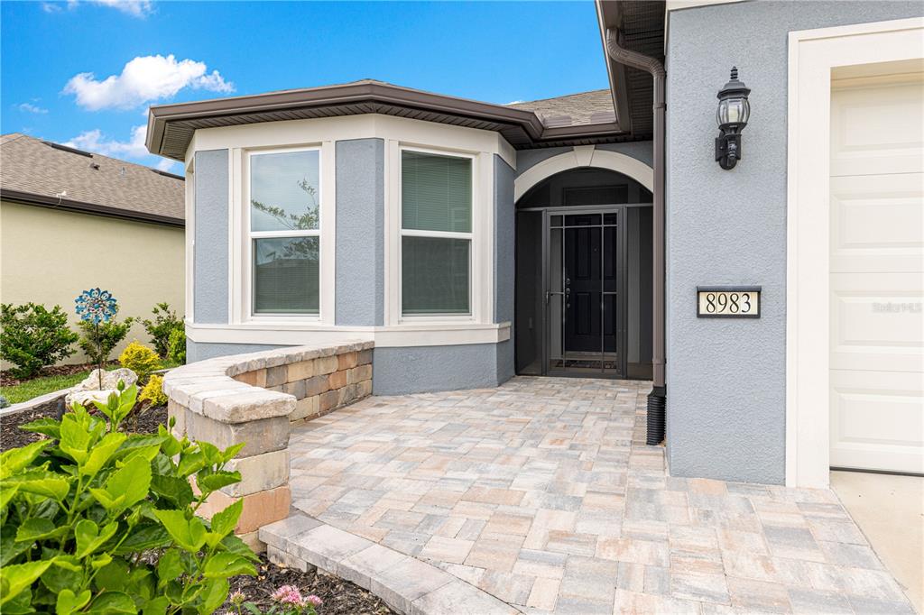 The exterior of a house features a paver patio, a stone retaining wall, and a front entrance — 8983 SW 57TH PLACE ROAD, OCALA, FL
