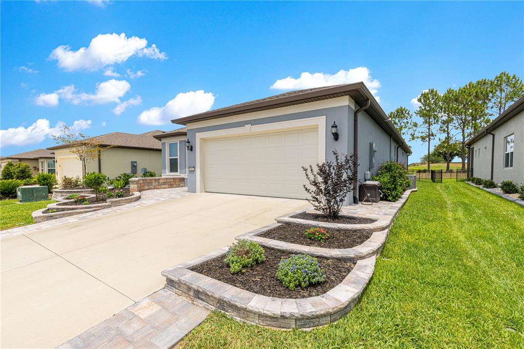 A gray house with a two-car garage and tiered stone-walled landscaping beds in the front — 8983 SW 57TH PLACE ROAD, OCALA, FL
