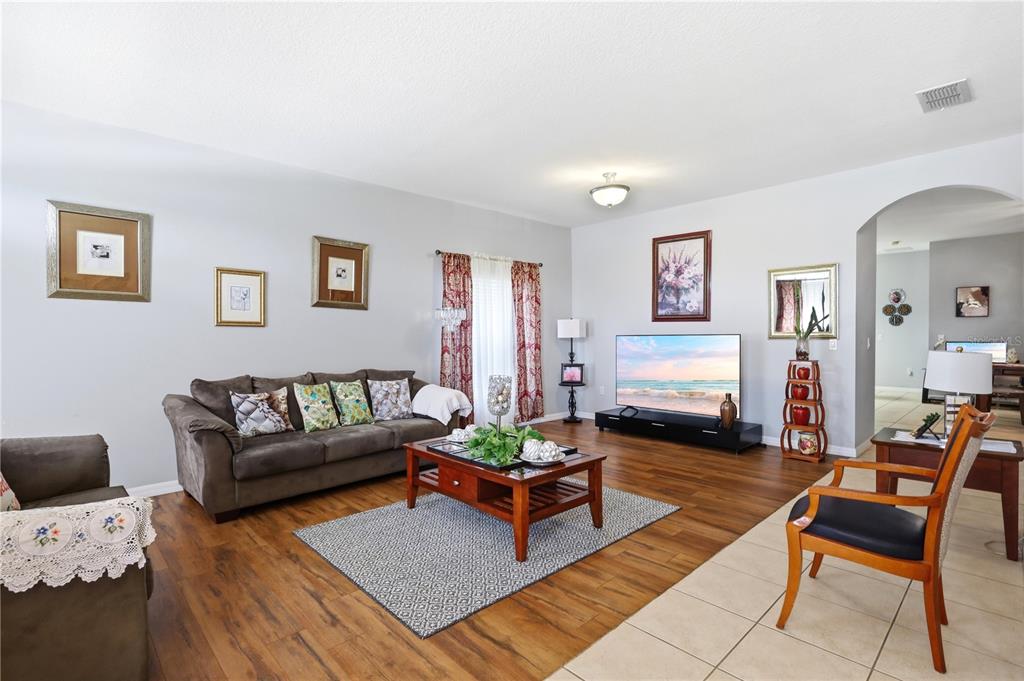 A living room features wood-look flooring, a brown sofa, a coffee table, and a television — 907 HACIENDA CIRCLE, KISSIMMEE, FL