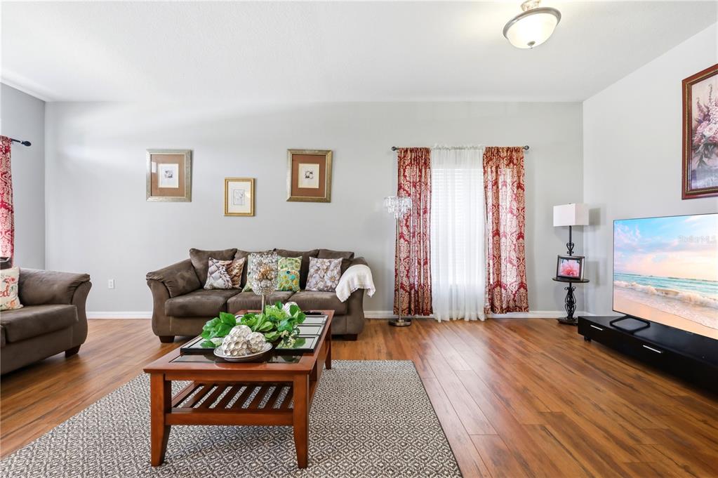 A living room features a brown sofa, a coffee table, and a television on wood floors — 907 HACIENDA CIRCLE, KISSIMMEE, FL
