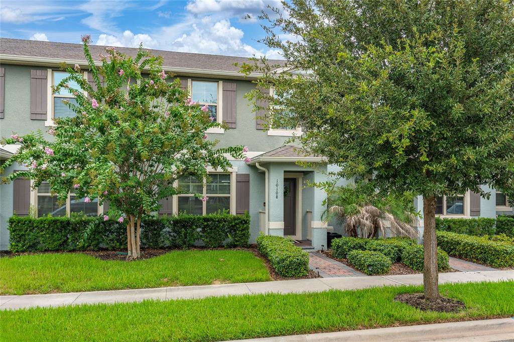 A two-story townhouse with a green stucco exterior, brown shutters, and a landscaped front yard — 10108 SALT POINT DRIVE, WINTER GARDEN, FL