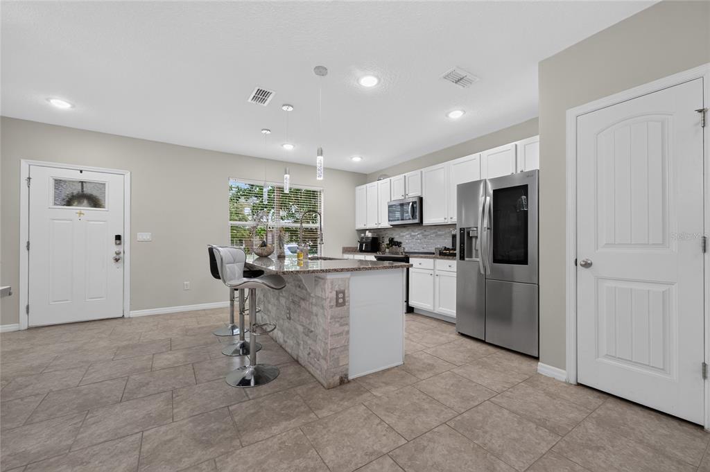 A kitchen with white cabinets, stainless steel appliances, a stone-faced island, and tile flooring — 10108 SALT POINT DRIVE, WINTER GARDEN, FL