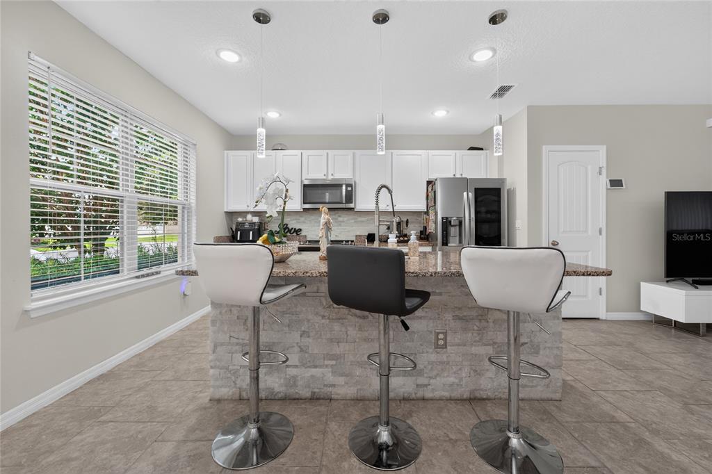 A kitchen features white cabinets, a stone-faced island with three bar stools, and tile flooring — 10108 SALT POINT DRIVE, WINTER GARDEN, FL