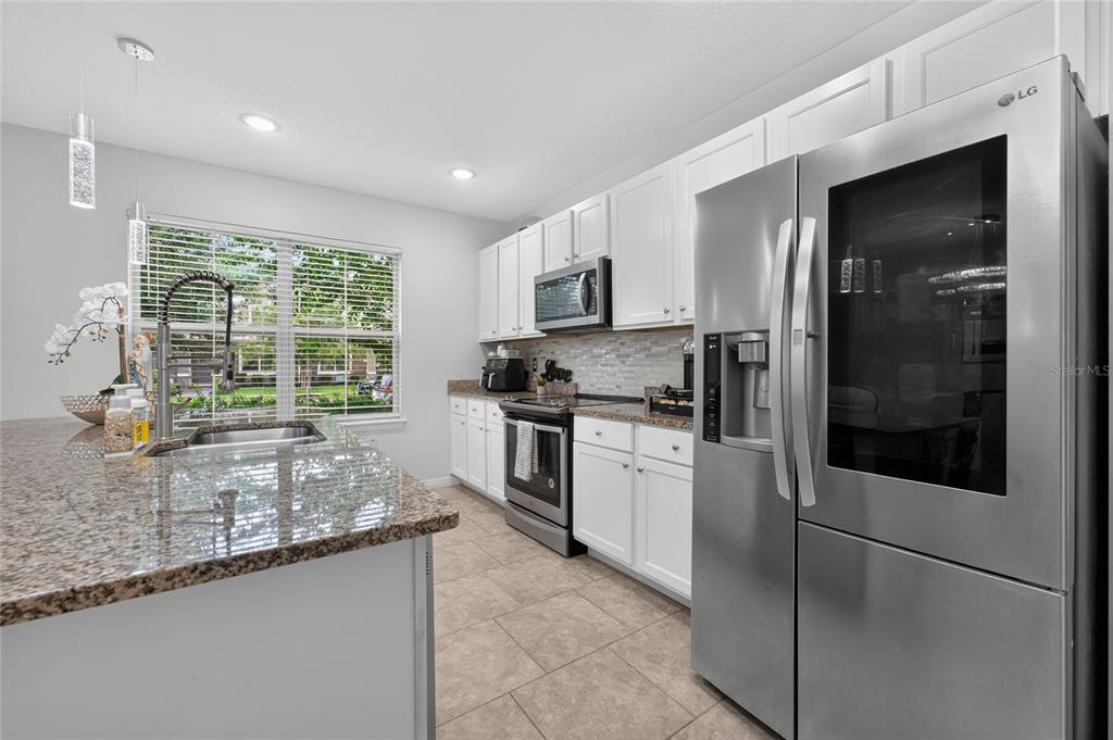 A kitchen features white cabinets, granite countertops, stainless steel appliances, and a large island — 10108 SALT POINT DRIVE, WINTER GARDEN, FL