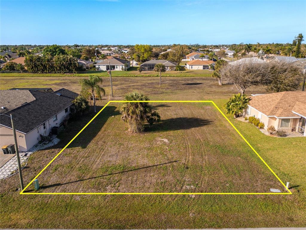 An aerial view shows a vacant residential lot outlined in yellow between two existing houses — 7179 N PLUM TREE, PUNTA GORDA, FL