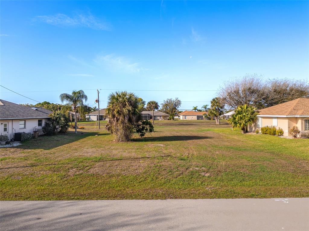 A vacant residential lot sits between two single-story houses under a clear blue sky — 7179 N PLUM TREE, PUNTA GORDA, FL