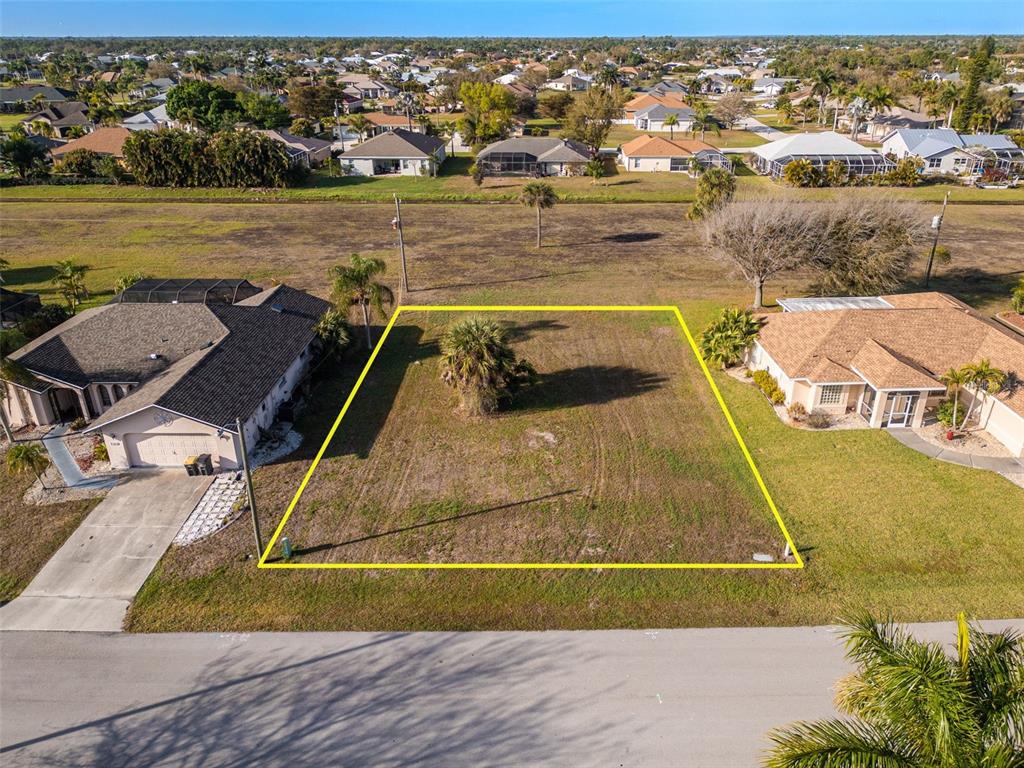 An aerial view shows a vacant residential lot outlined in yellow between two houses — 7179 N PLUM TREE, PUNTA GORDA, FL