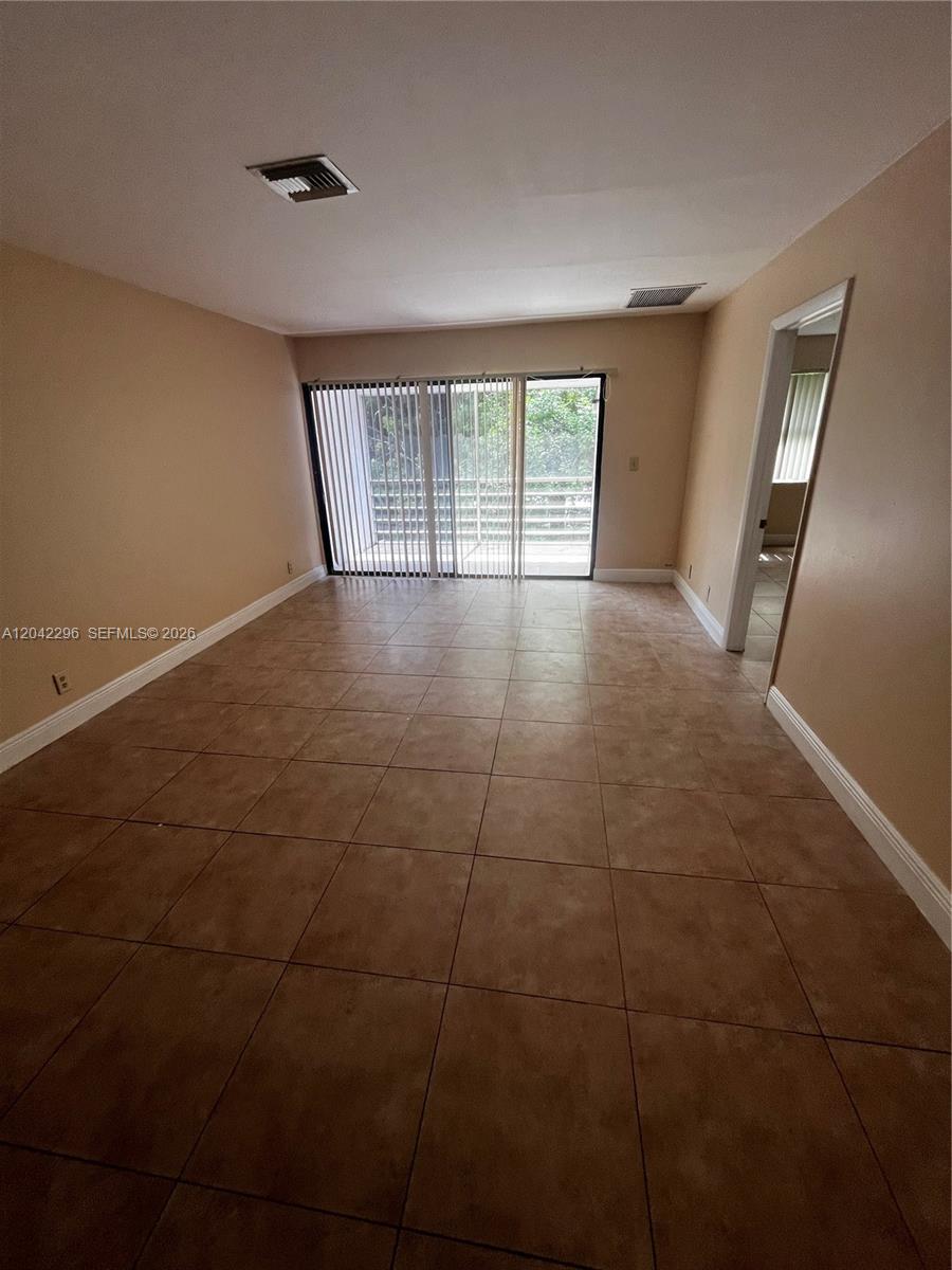 An empty room features tan tile flooring, beige walls, and a sliding glass door — 7830 NW 33rd St # 206, Davie FL 33024, DAVIE, FL