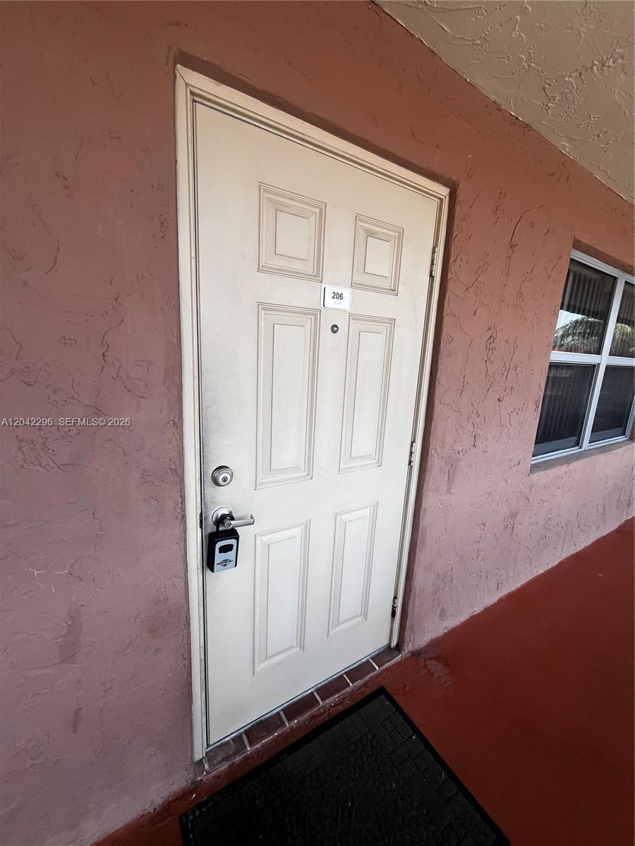 A white exterior door with a lockbox is set into a textured, salmon-colored wall — 7830 NW 33rd St # 206, Davie FL 33024, DAVIE, FL