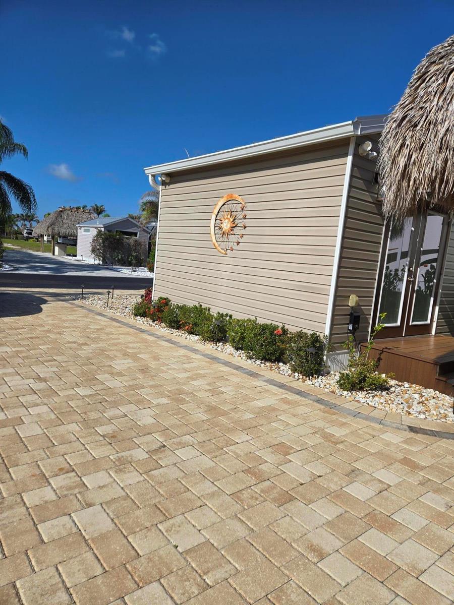 A beige mobile home exterior features a sun wall decoration, landscaping, and a paver driveway — 639 34th Trace SW, Okeechobee FL 34974, OKEECHOBEE, FL