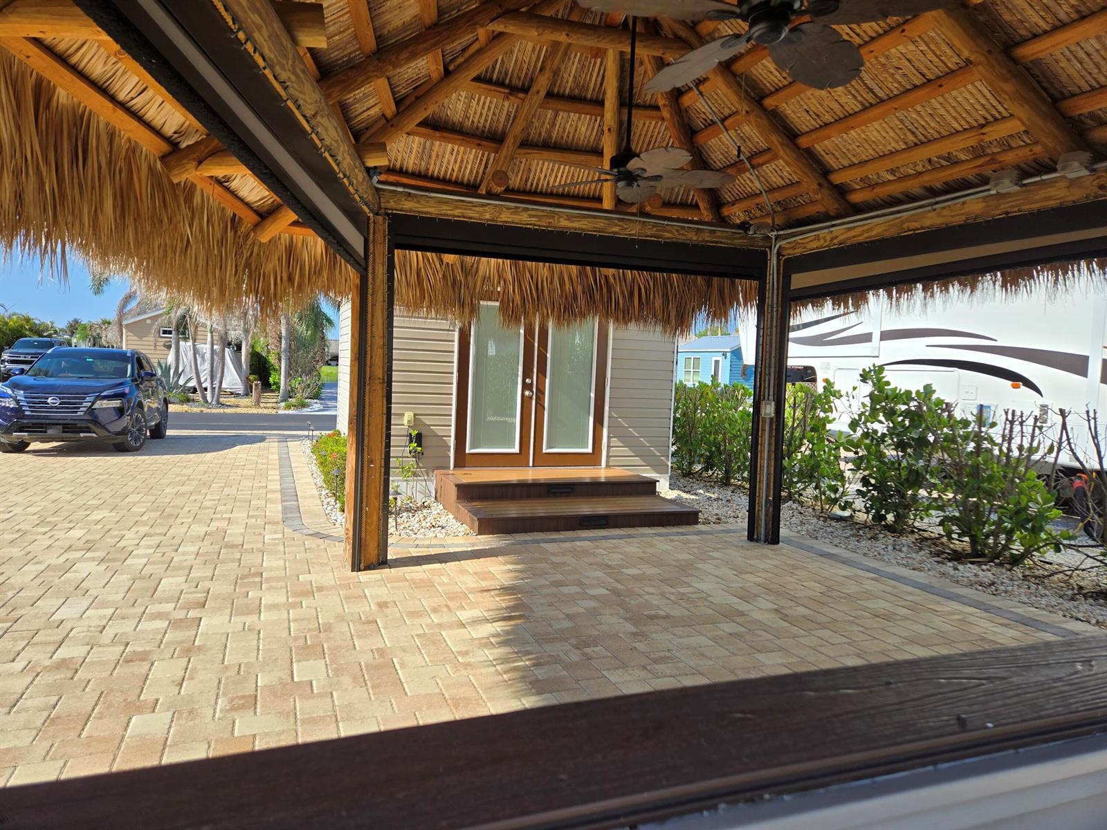 A thatched-roof tiki hut overlooks a paved patio, a small building, and a parked car — 639 34th Trace SW, Okeechobee FL 34974, OKEECHOBEE, FL