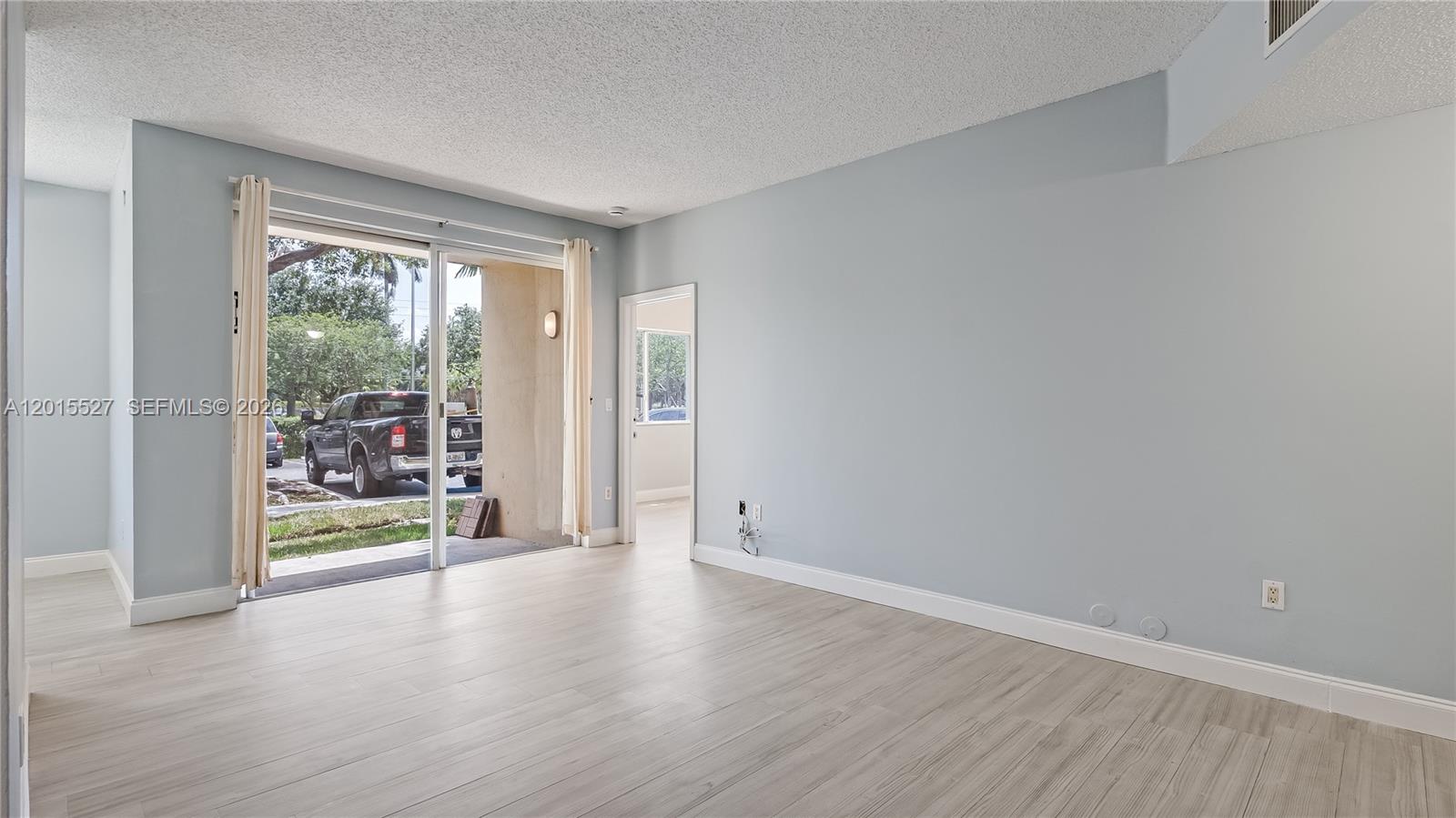 A living room with light blue walls, wood-look flooring, and a sliding glass door — 7085 Nova Dr # 105, Davie FL 33317, DAVIE, FL