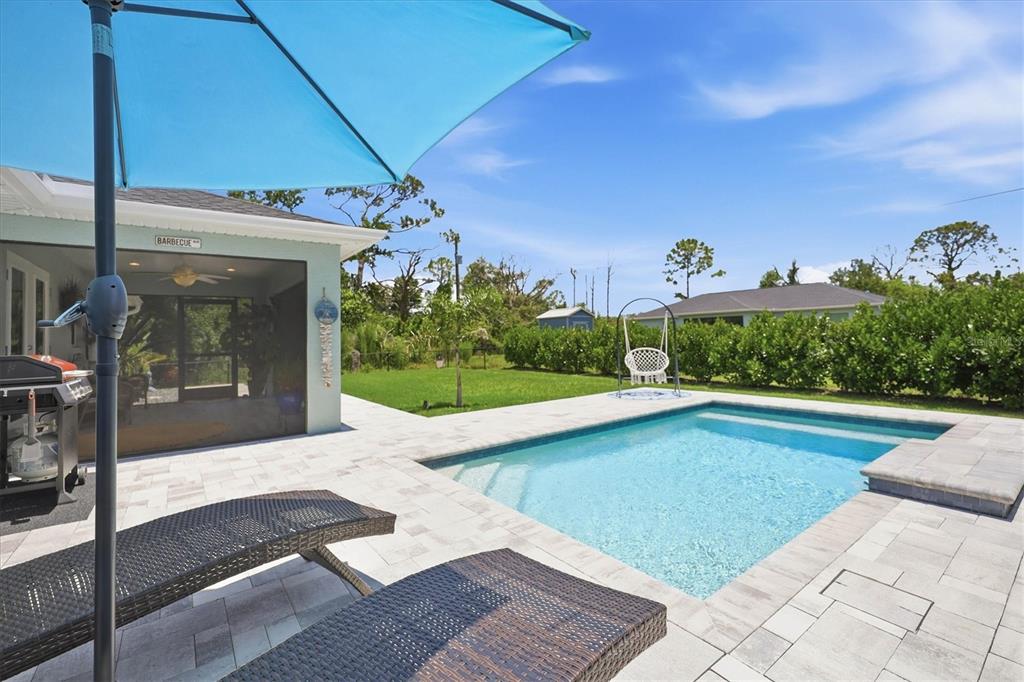 A backyard features a swimming pool, lounge chairs, a patio umbrella, and a covered porch — 14175 STACKS AVENUE, PORT CHARLOTTE, FL