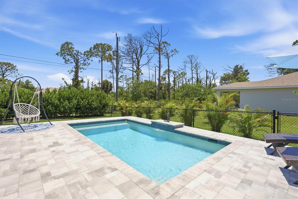 A rectangular swimming pool with a stone patio and a hanging chair in a backyard — 14175 STACKS AVENUE, PORT CHARLOTTE, FL