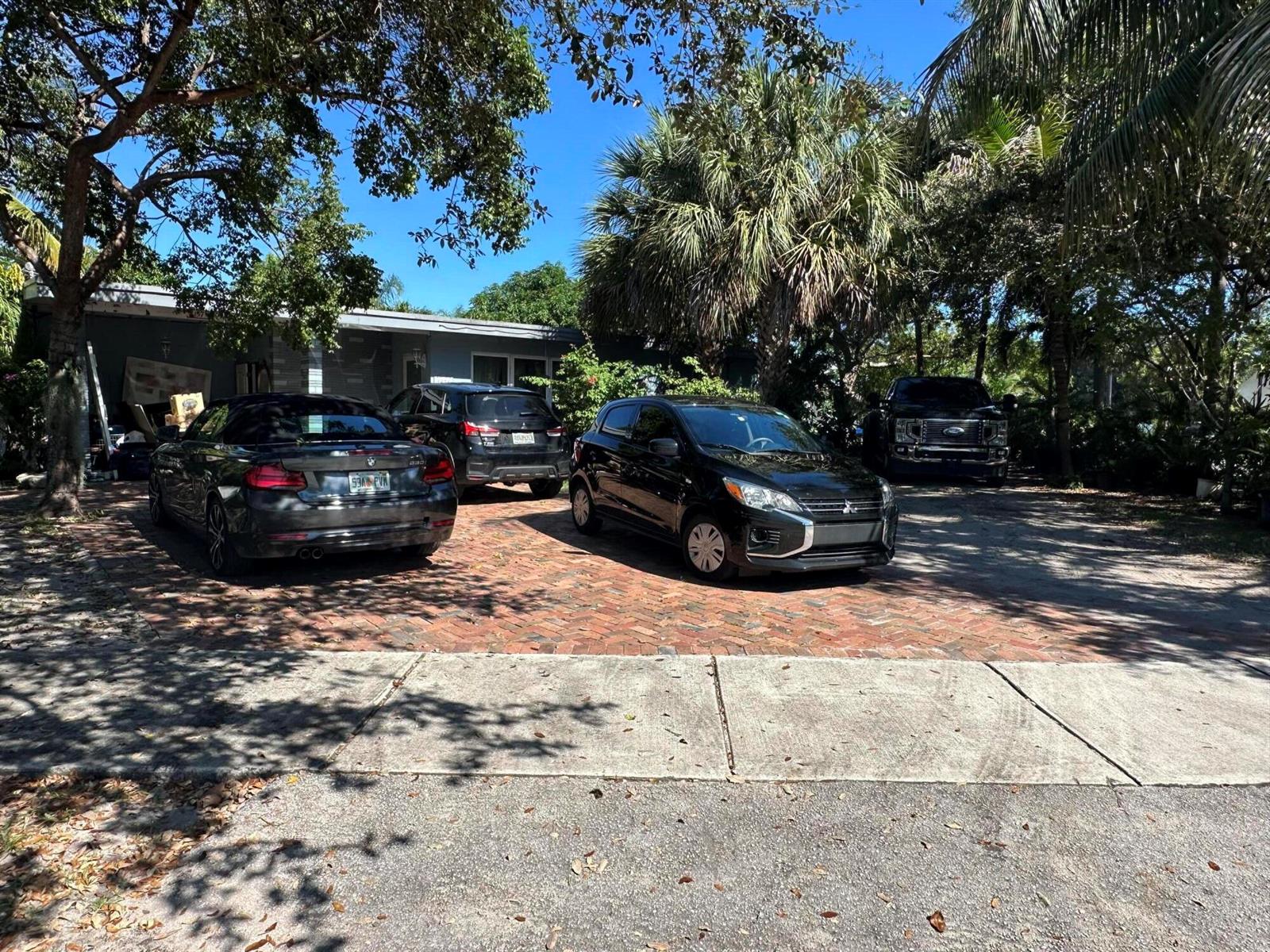 A brick driveway in front of a house features four parked vehicles under trees — 1571 NE 43rd Street, Pompano Beach FL 33064, POMPANO BEACH, FL