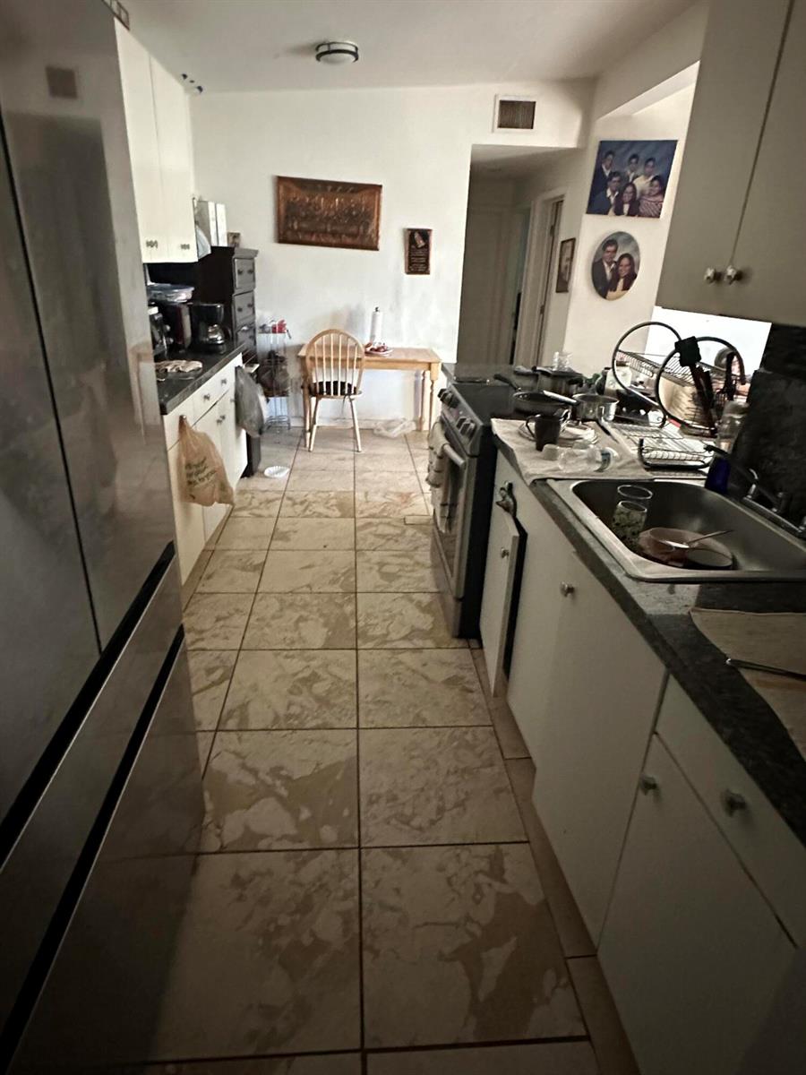 A galley kitchen features white cabinets, dark countertops, and light-colored tile flooring — 1571 NE 43rd Street, Pompano Beach FL 33064, POMPANO BEACH, FL