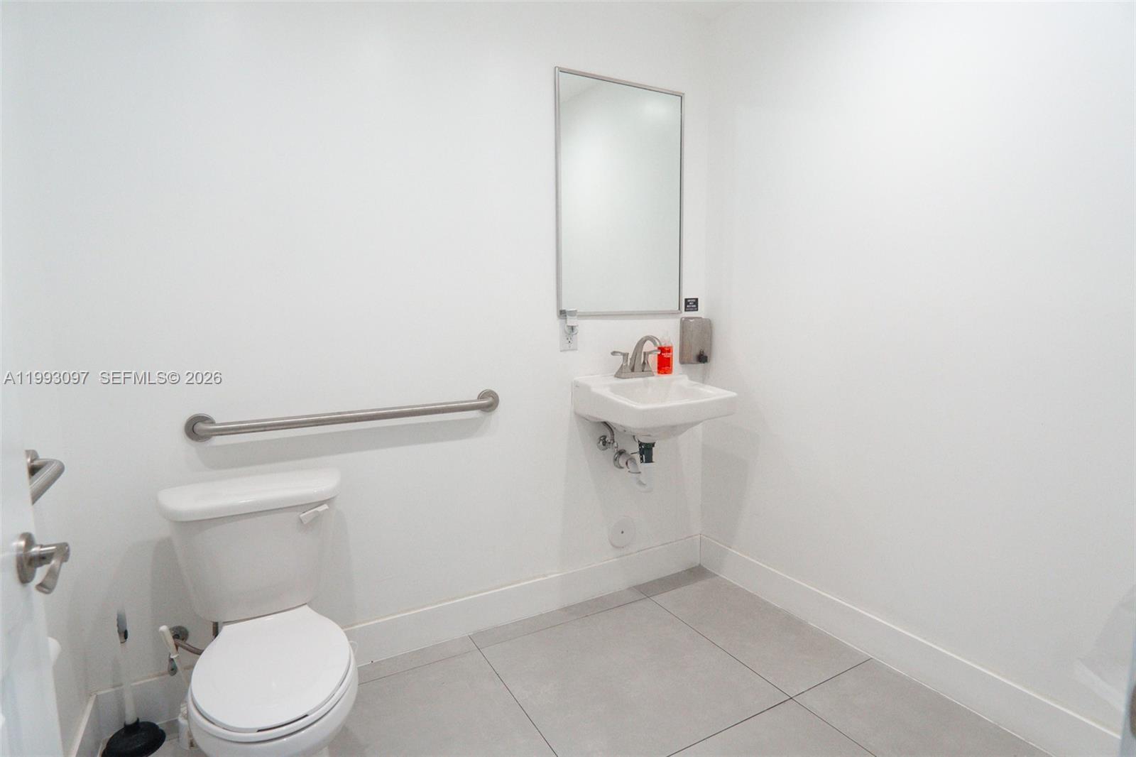 A minimalist bathroom features a white toilet, a wall-mounted sink, and a grab bar — 2268 SW 8th St, Miami FL 33135, MIAMI, FL