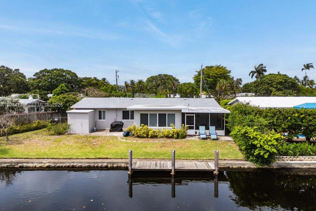 An exterior view of a single-story house with a backyard, wooden dock, and canal — 509 NE 29th St, Wilton Manors FL 33334, WILTON MANORS, FL