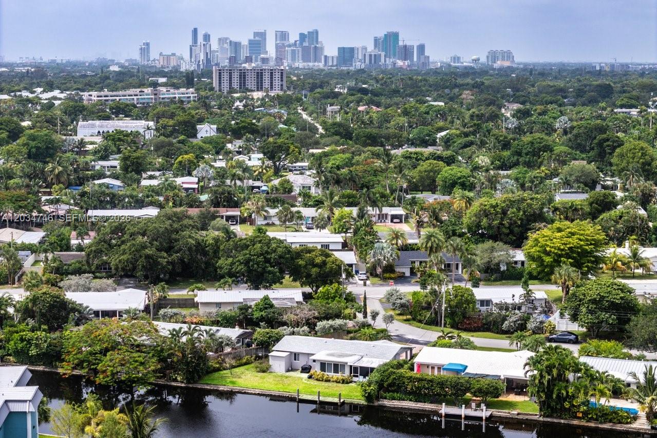 An aerial view shows a residential neighborhood with lush trees, a canal, and a distant skyline — 509 NE 29th St, Wilton Manors FL 33334, WILTON MANORS, FL