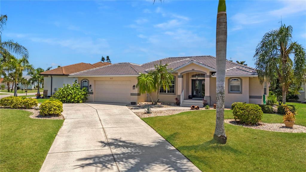 A single-story house with a beige exterior, a two-car garage, and a palm-lined front yard — 527 SAINT GIRONS COURT, PUNTA GORDA, FL
