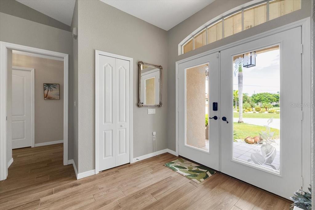 An entryway features light wood-look flooring, a white double door, and a small wall mirror — 527 SAINT GIRONS COURT, PUNTA GORDA, FL