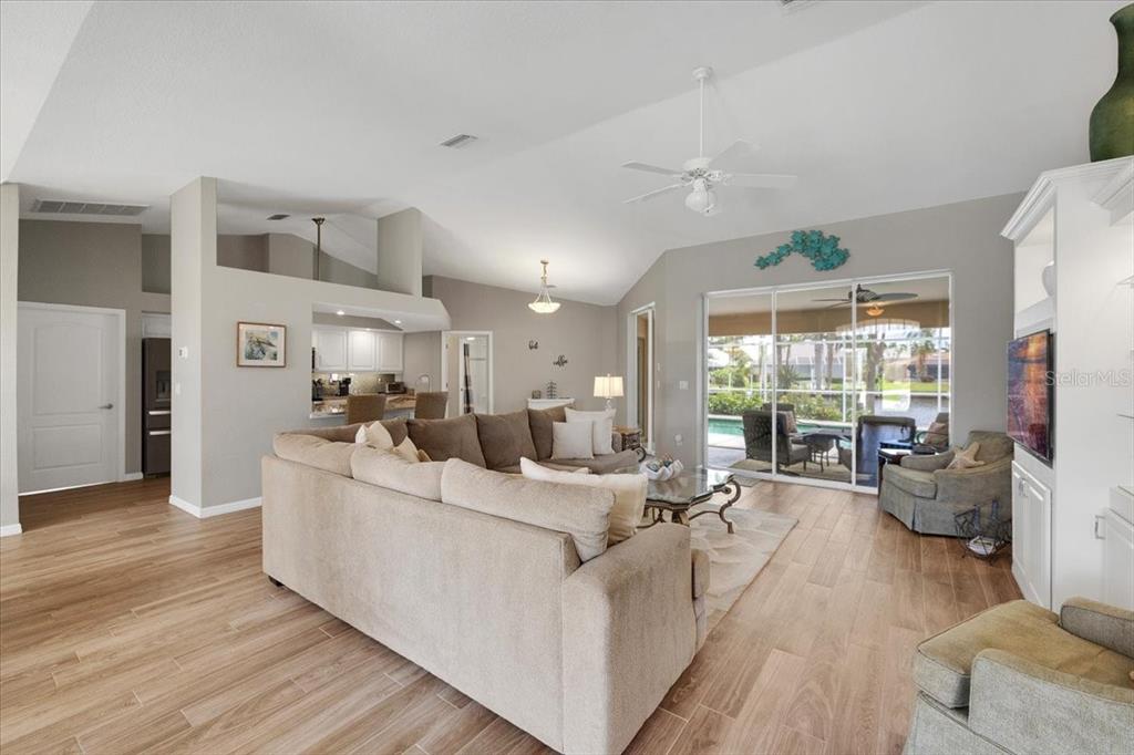 A living room features light wood-look flooring, a large sectional sofa, and sliding glass doors — 527 SAINT GIRONS COURT, PUNTA GORDA, FL