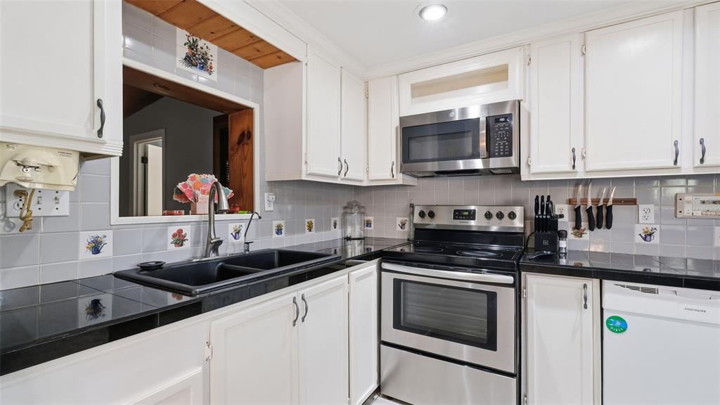 A kitchen features white cabinets, black countertops, stainless steel appliances, and a tiled backsplash — 10565 BESSEMER STREET, NEW PORT RICHEY, FL