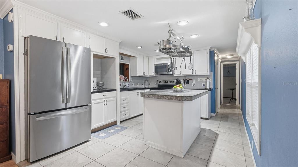 A kitchen features white cabinetry, stainless steel appliances, a granite-topped island, and light tile flooring — 10565 BESSEMER STREET, NEW PORT RICHEY, FL