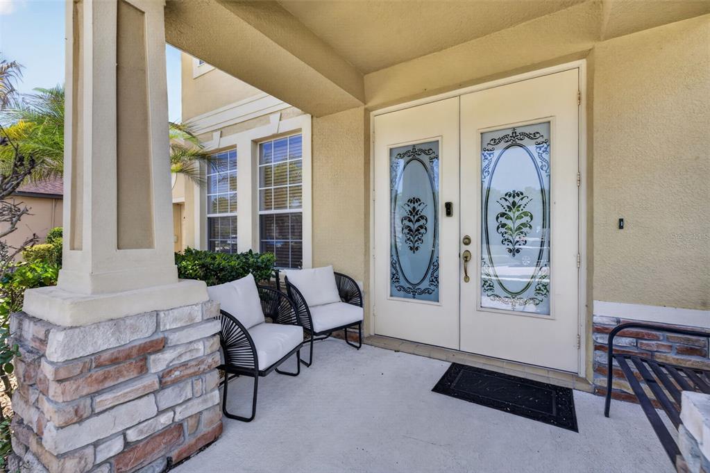 A covered front porch features two modern chairs, a bench, and double glass-paneled doors — 7438 CHELSEA HARBOUR DRIVE, ORLANDO, FL
