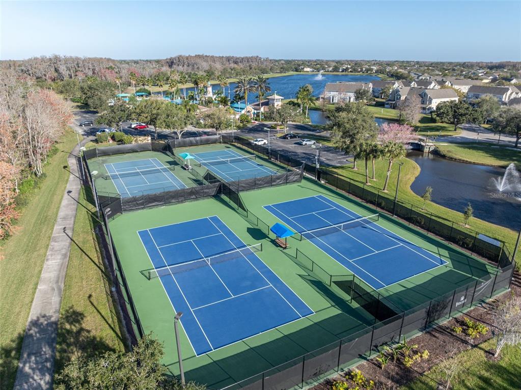 An aerial view shows four blue tennis courts surrounded by fencing near a lake — 7438 CHELSEA HARBOUR DRIVE, ORLANDO, FL