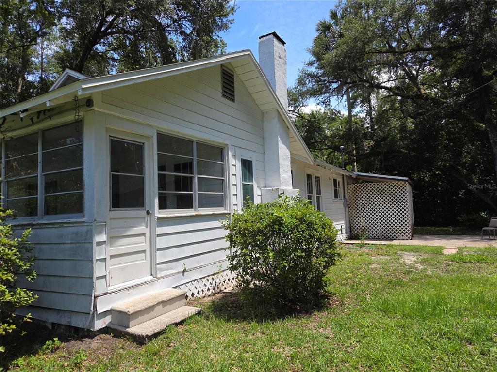 A white house with a chimney, screened porch, and lattice-covered patio sits in a yard — 11280 NE HIGHWAY 314, SILVER SPRINGS, FL