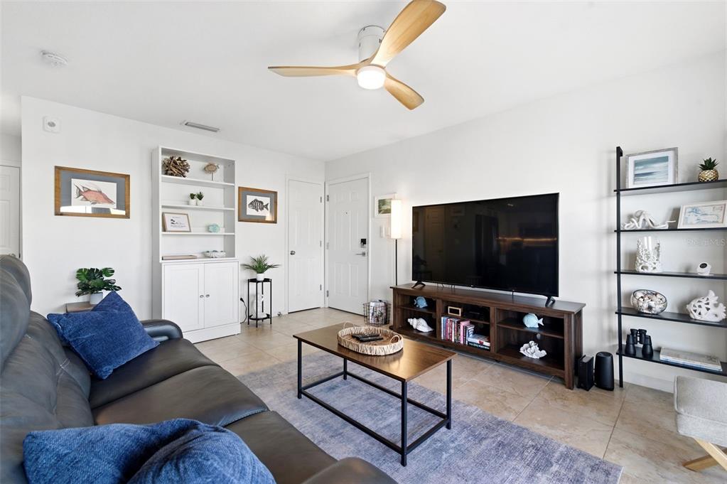 A living room features a dark leather sofa, a television on a wooden stand, and shelving — 5174 BEACH DRIVE SE UNIT D, ST PETERSBURG, FL