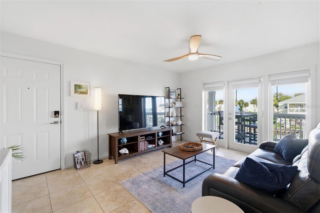 A living room features a television, a dark leather sofa, and a glass door balcony — 5174 BEACH DRIVE SE UNIT D, ST PETERSBURG, FL