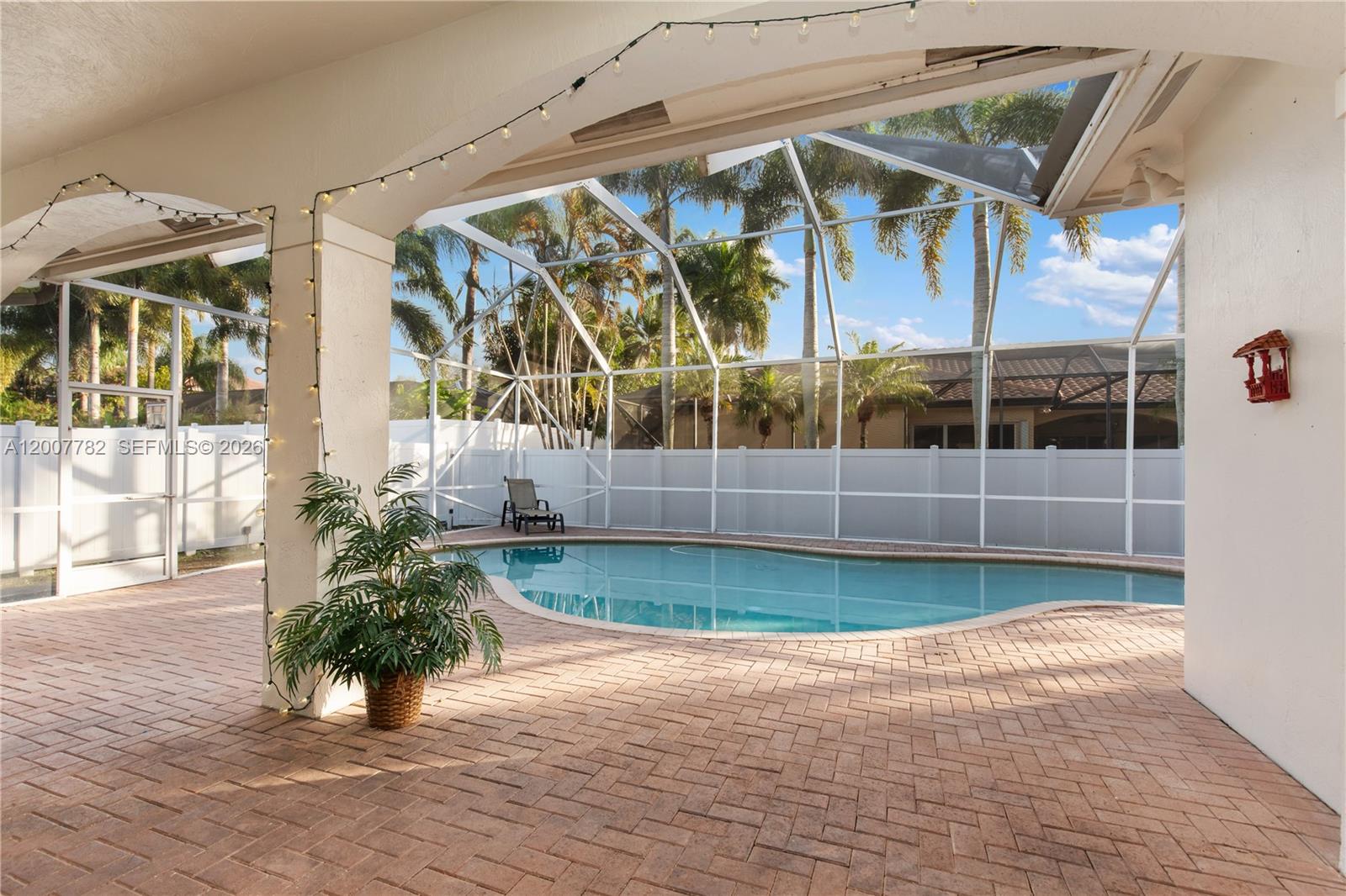 A covered patio with brick pavers overlooks a screened-in swimming pool and palm trees — 15966 SW 3rd St, Pembroke Pines FL 33027, PEMBROKE PINES, FL