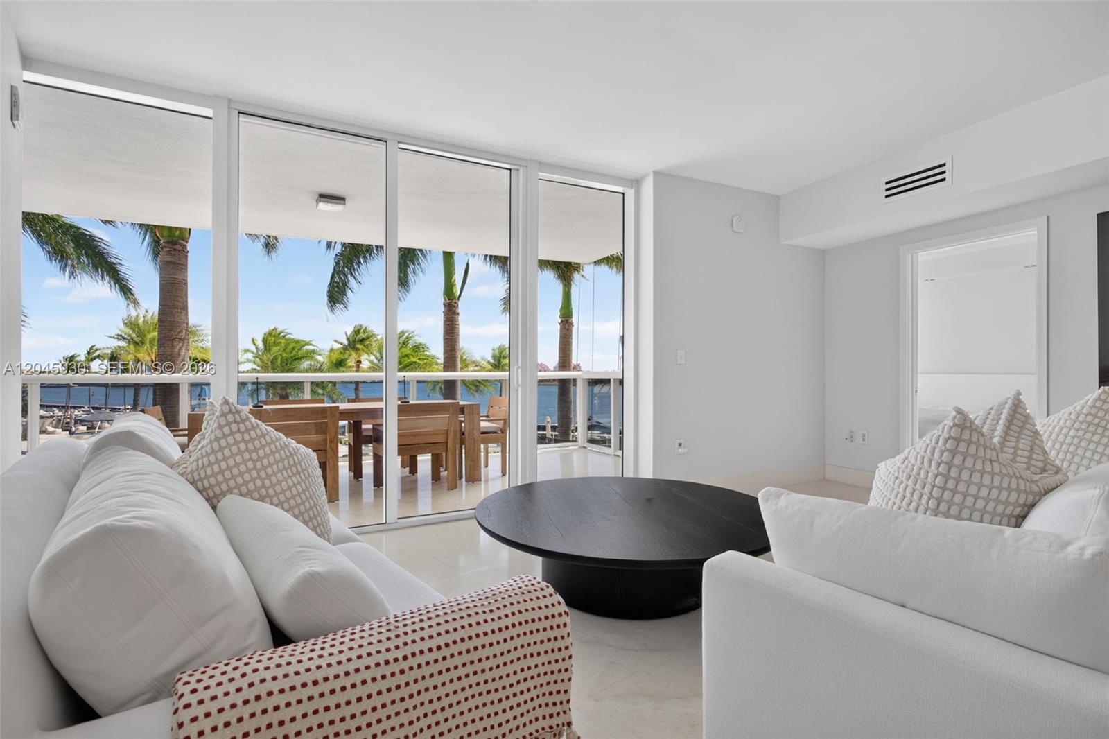 A bright living room features two white sofas, a black oval coffee table, and dining area — 400 Alton Rd # 706, Miami Beach FL 33139, MIAMI BEACH, FL