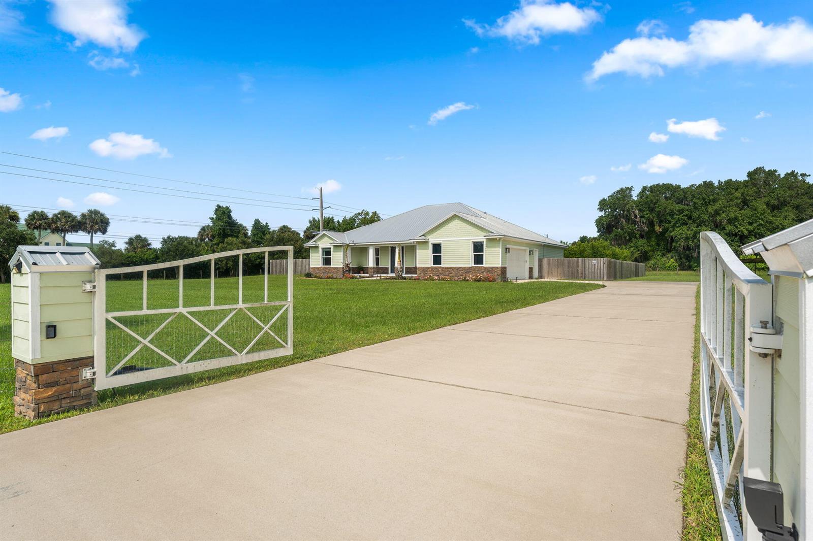 A light green house with a metal roof sits behind an open metal gate — 2520 Tammy Drive, Mims FL 32754, MIMS, FL